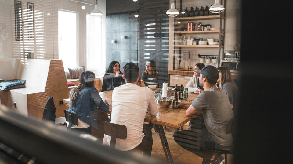 Une équipe échange autour d'une grande table, vue à travers une paroi vitrée