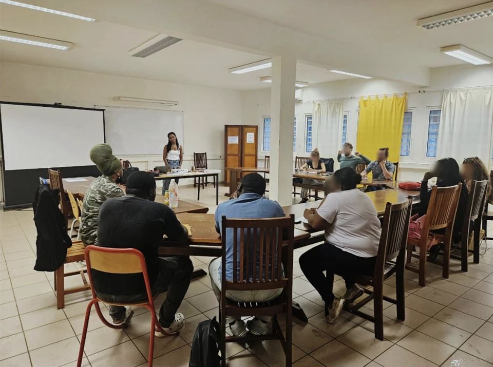 Une formatrice anime une séance devant des participants installés autour de tables, dans une salle de formation